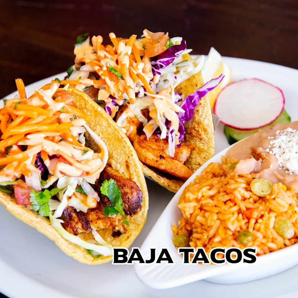 Two Baja tacos with shredded cabbage, carrots, and sauce, served with rice and beans.