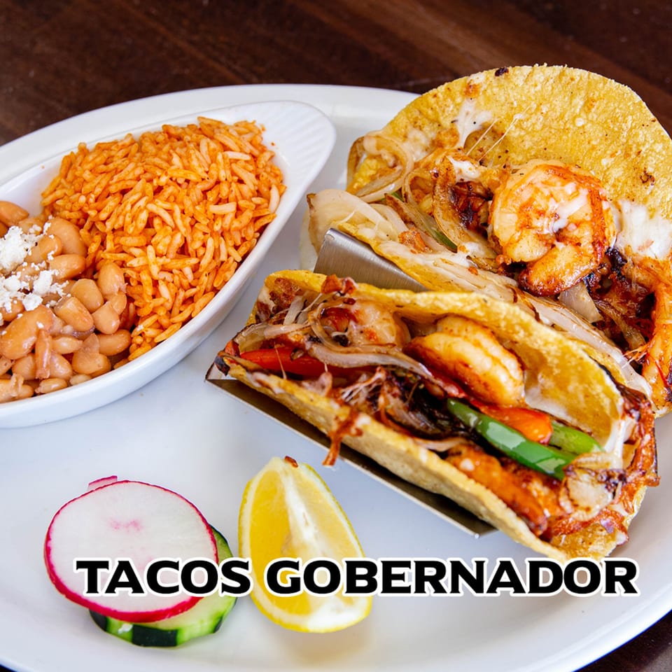 Two shrimp tacos with melted cheese, rice, beans, radish, and lemon on a white plate.