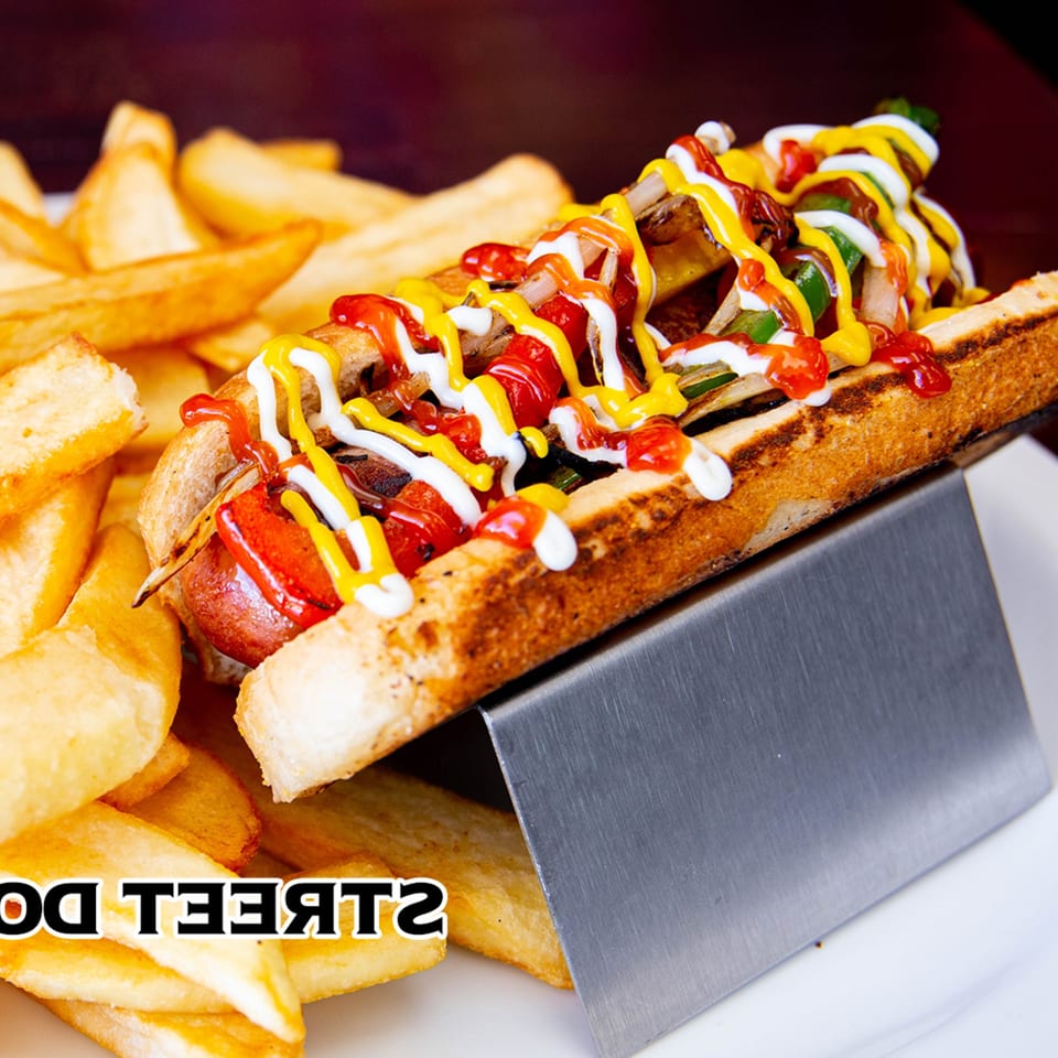 A House of Tacos Grill hot dog with ketchup, mustard, and mayonnaise, served with fries.