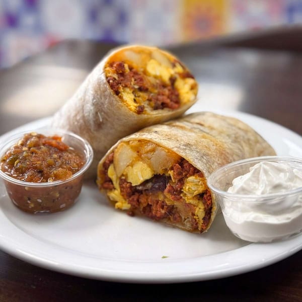 Two House of Tacos Grill burritos, cut in half, with sides of salsa and sour cream.