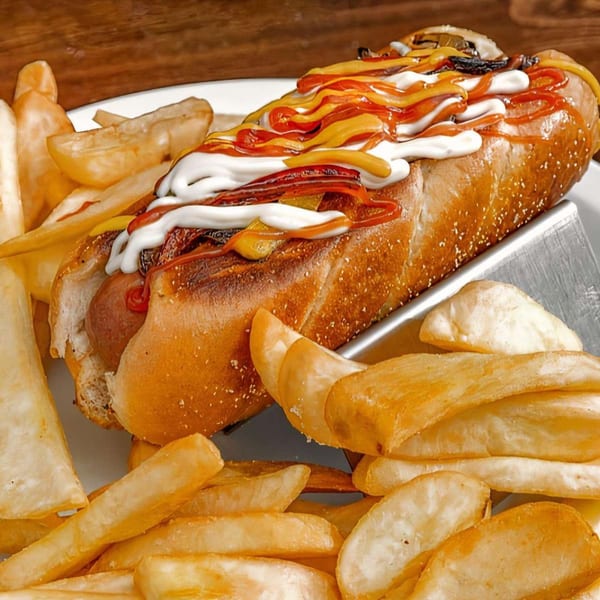 A hot dog with ketchup, mustard, and mayonnaise, served with a side of golden french fries.
