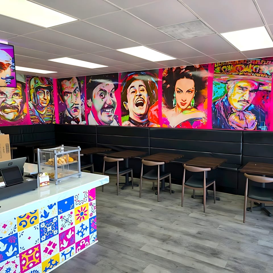 Interior of House of Tacos Grill with colorful pop art murals, black booths, and a tiled counter.