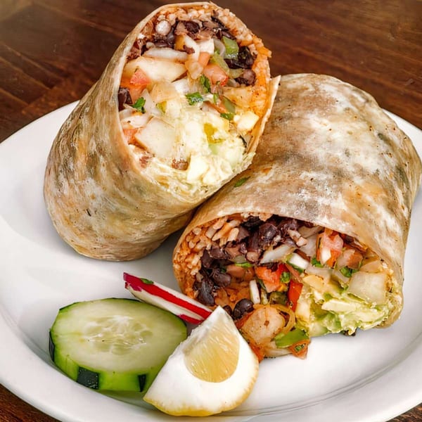 Two large burritos, cut in half, revealing rice, beans, and vegetables, with a lemon wedge and cucumber.