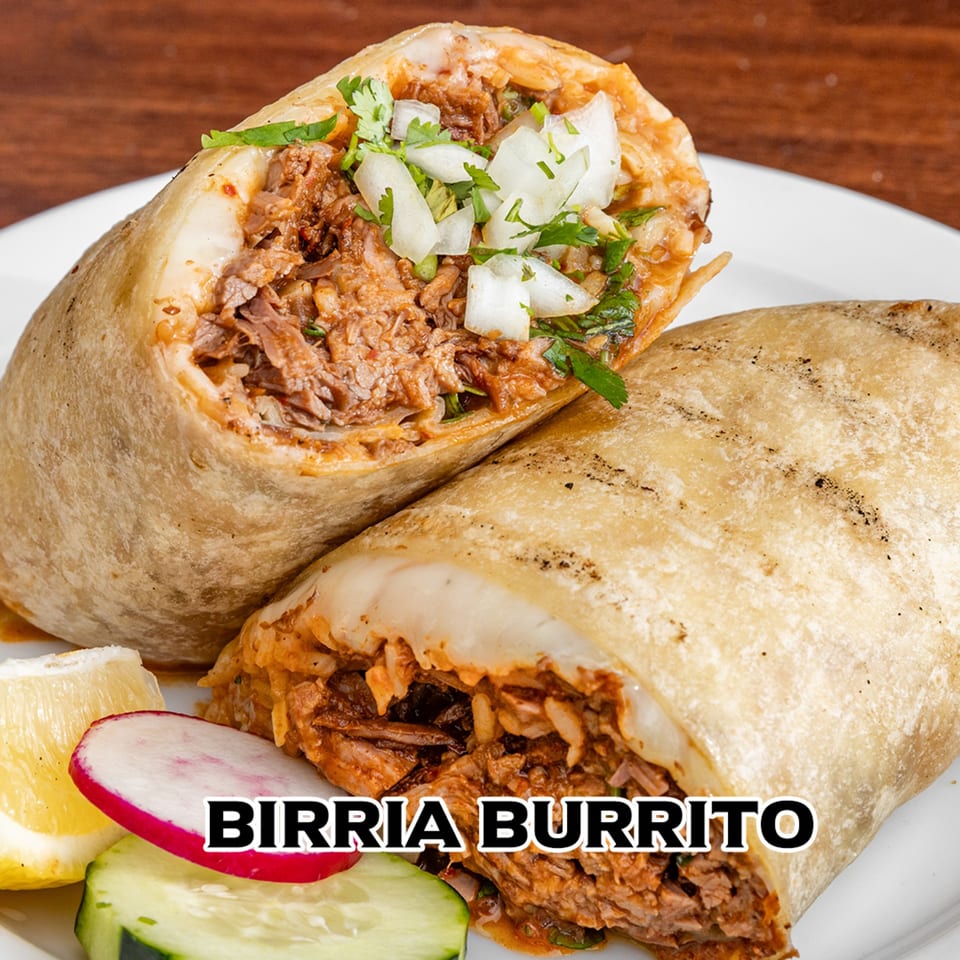 Two birria burritos, one cut open to show shredded meat, onions, and cilantro, with lemon, radish, and cucumber.