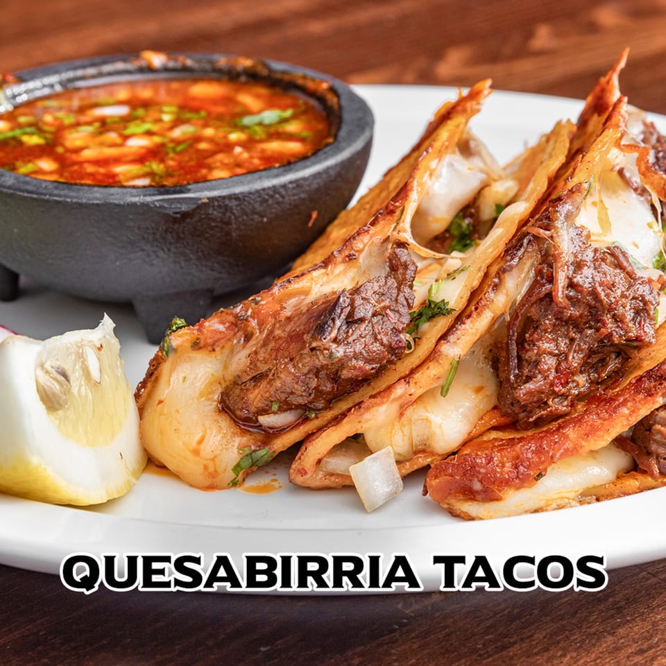 Three quesabirria tacos with melted cheese and meat, served with a side of consommé and a lemon wedge.