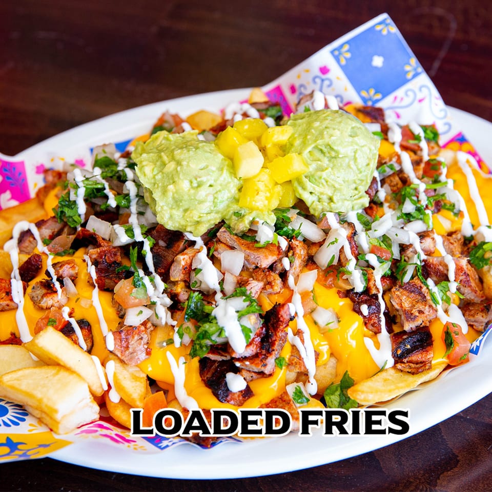 Loaded fries with cheese, carne asada, guacamole, and pico de gallo on a white plate.