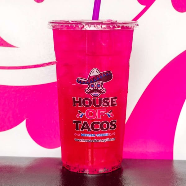 Bright pink drink with a purple straw in a House of Tacos branded cup.