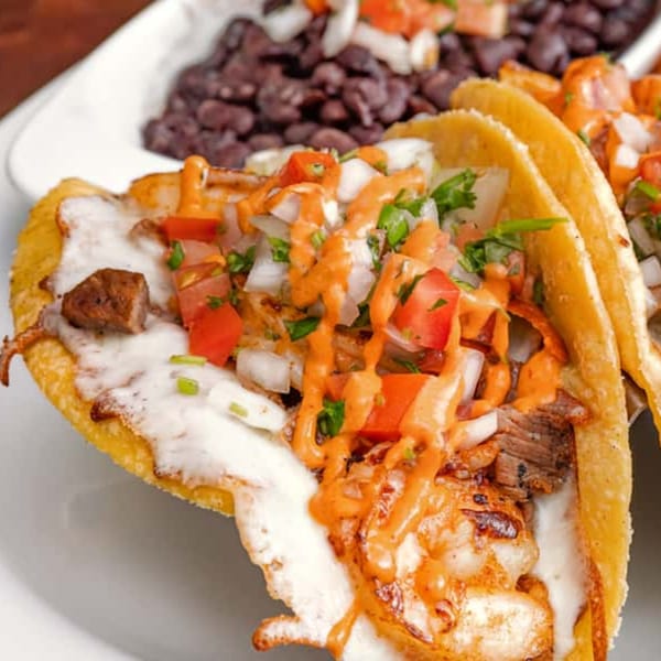 Two House of Tacos Grill tacos with meat, pico de gallo, and sauce, served with black beans.