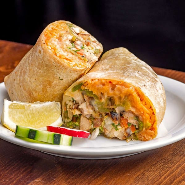 Two halves of a House of Tacos Grill burrito, filled with meat, rice, and vegetables, with lime and cucumber.